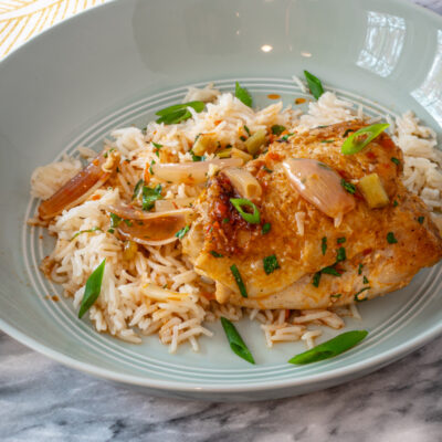 easy harissa chicken thighs shown with green onion garnish on rice