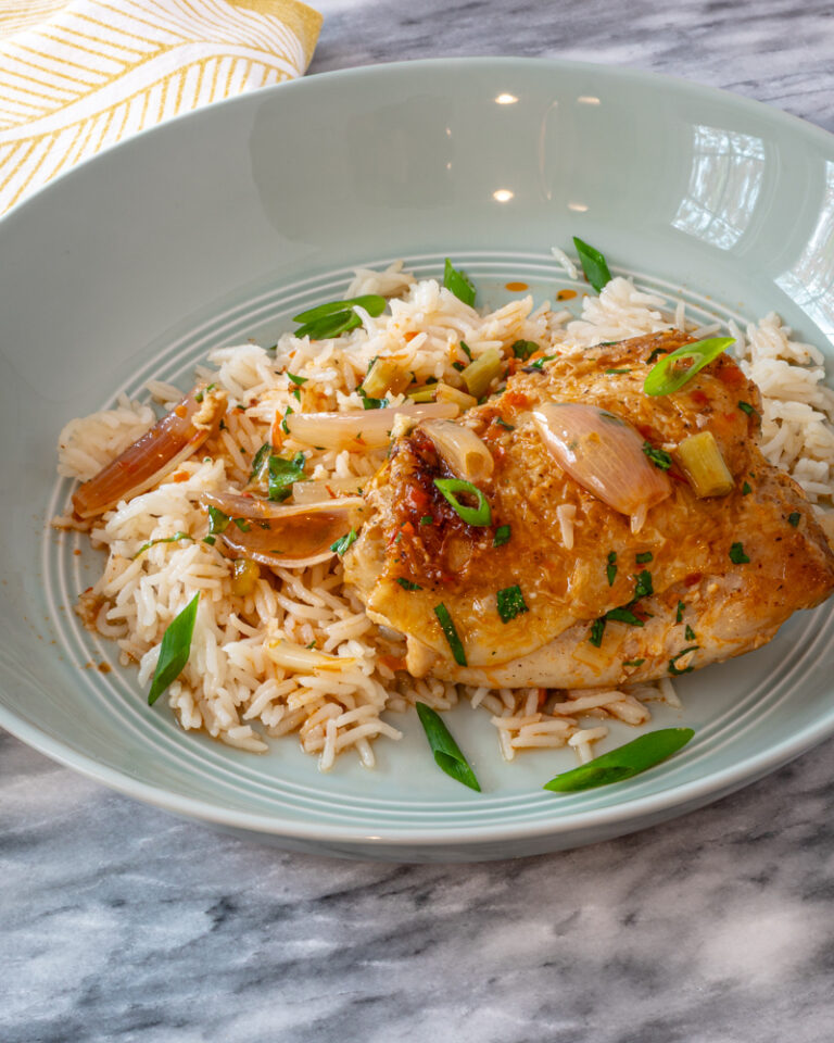 easy harissa chicken thighs shown with green onion garnish on rice