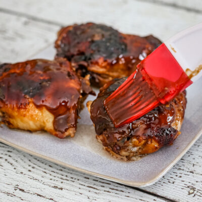 Brushing honey and peanut glaze over baked chicken thighs.