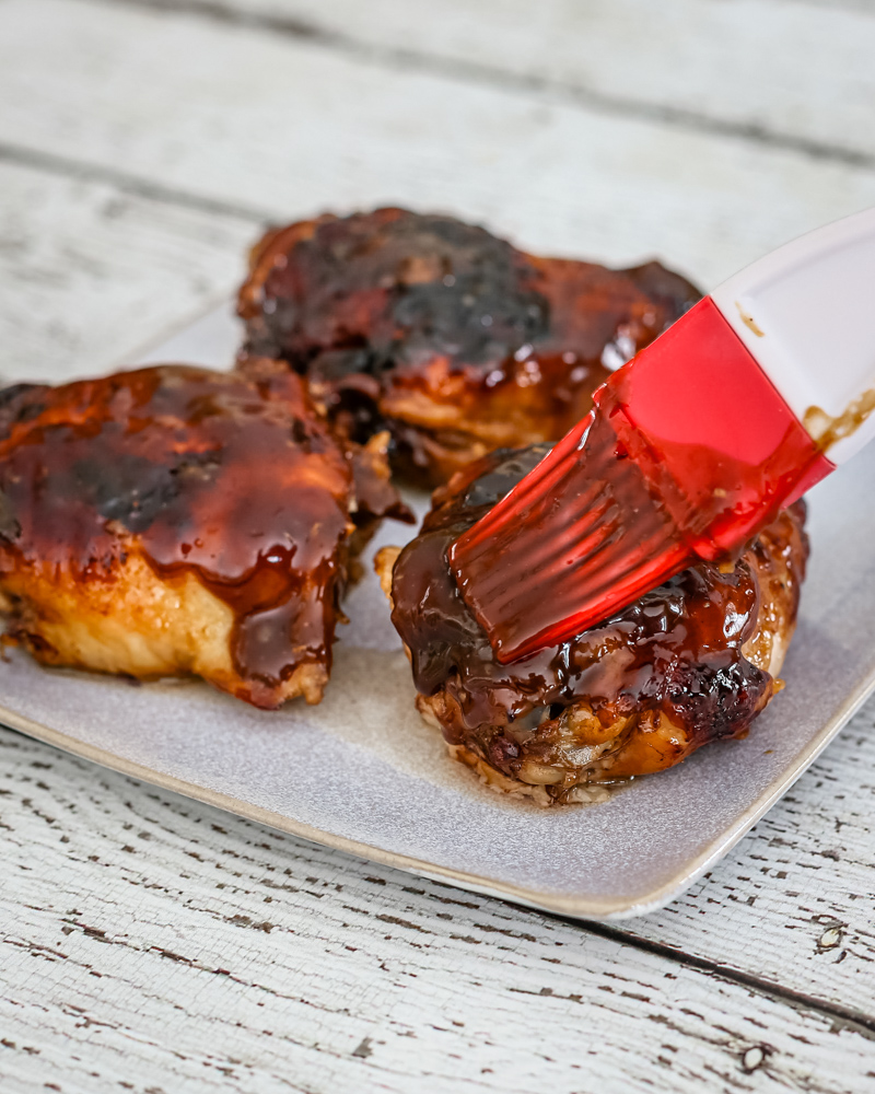 Brushing honey and peanut glaze over baked chicken thighs.