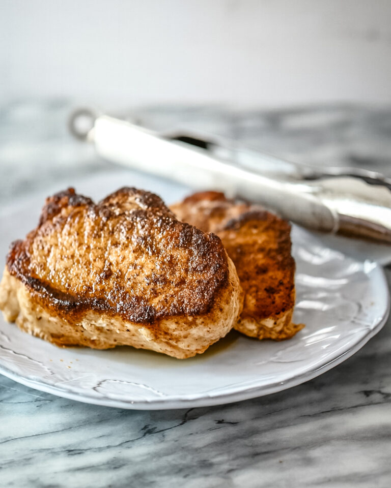 Instant Pot pressure cooker pork chops on a serving plate with tongs in the background.