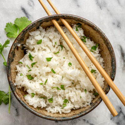 Steamed white rice garnished with fresh herbs in a rustic bowl.