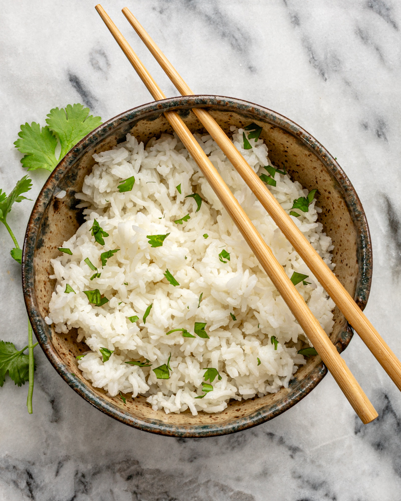 Steamed white rice garnished with fresh herbs in a rustic bowl.