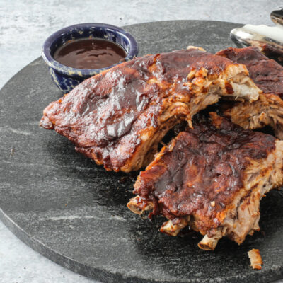 Baby back ribs on a marble serving board with extra bbq sauce.