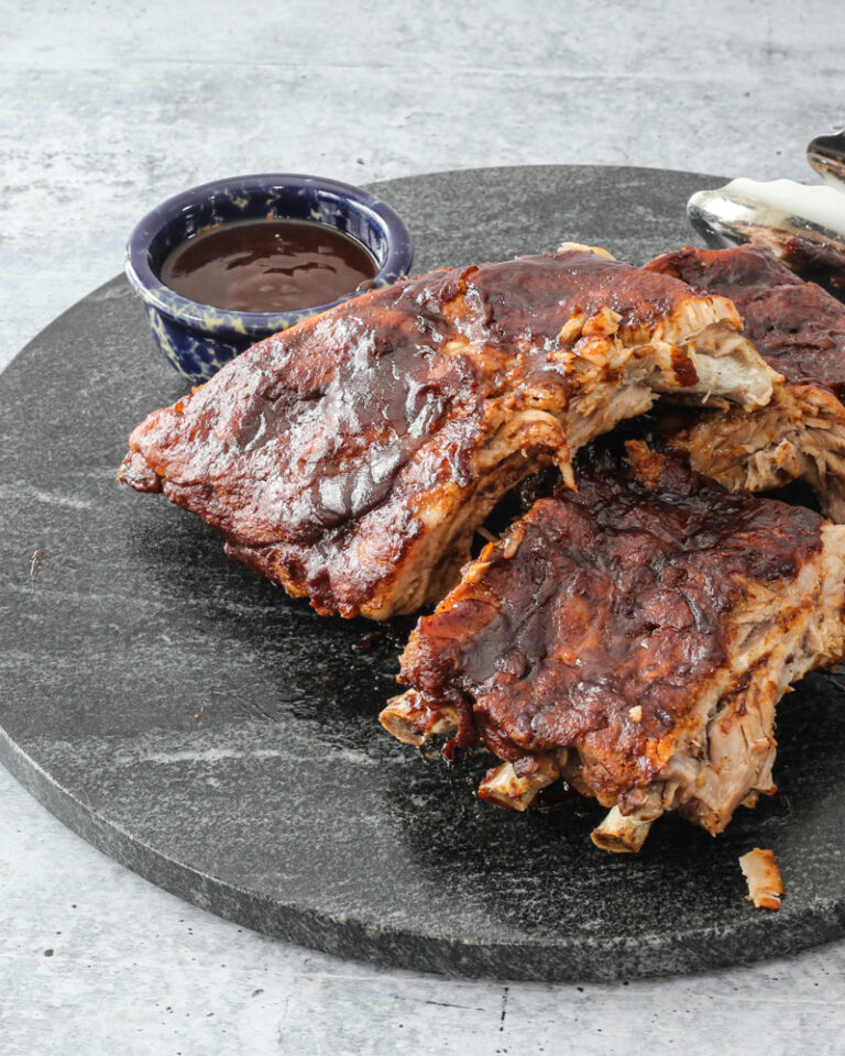 Baby back ribs on a marble serving board with extra bbq sauce.