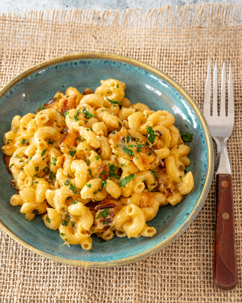 Creamy bacon macaroni and cheese with chopped herbs on top.