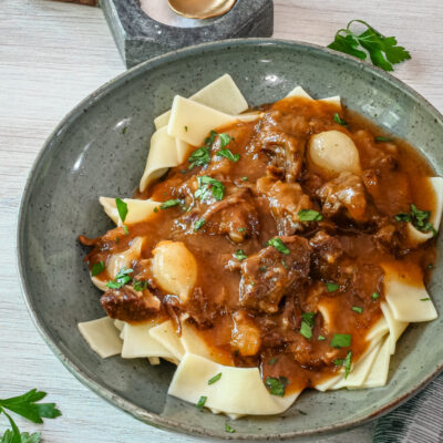 A serving of beef and beer stew on pasta, with parsley garnish.