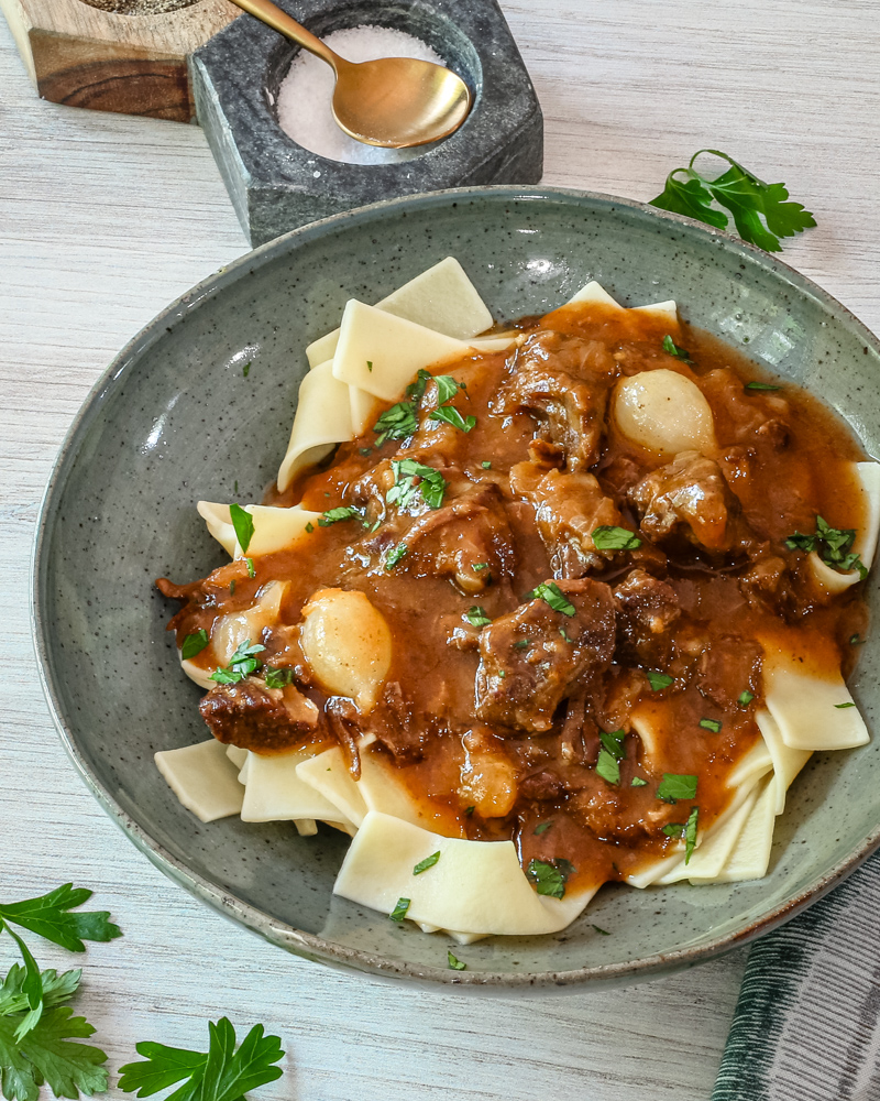 A serving of beef and beer stew on pasta, with parsley garnish.