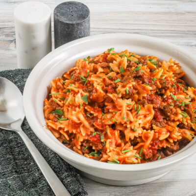 Bowl of farfalle with a beefy tomato sauce, and a place setting on the side.