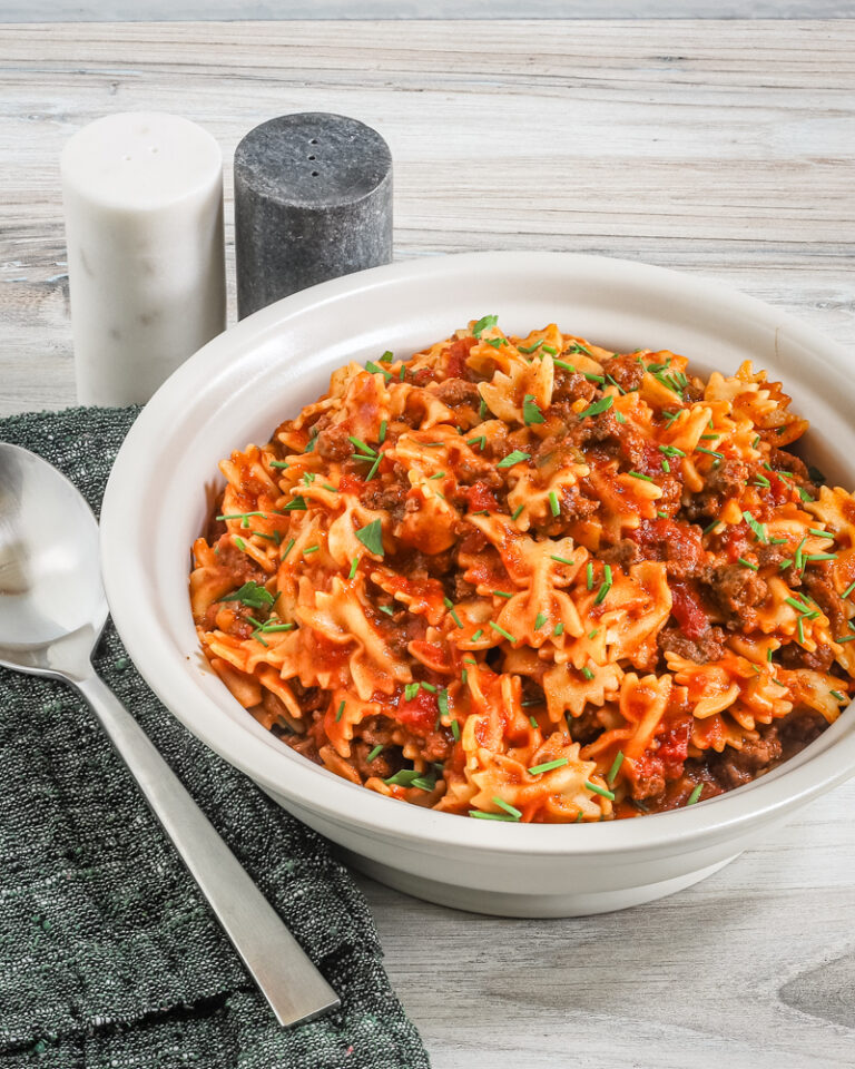 Bowl of farfalle with a beefy tomato sauce, and a place setting on the side.