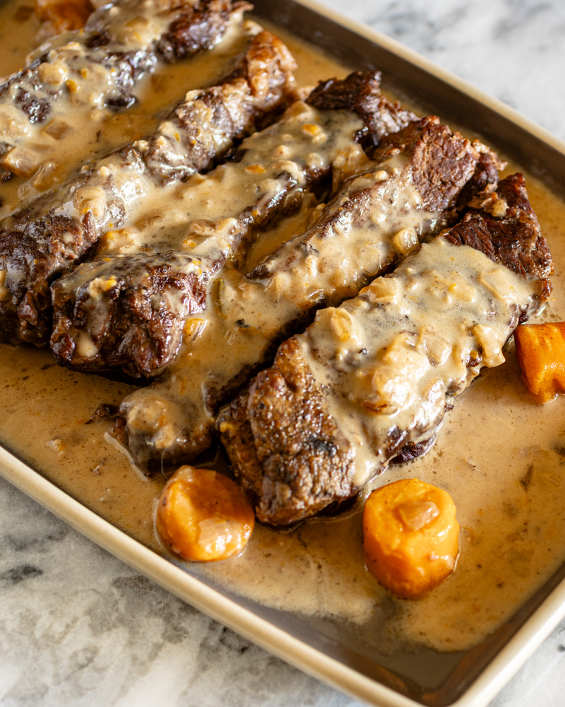Instant Pot beef short ribs on a serving tray with carrots and sauce.