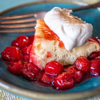A slice of cherry upside down cake with whipped cream.