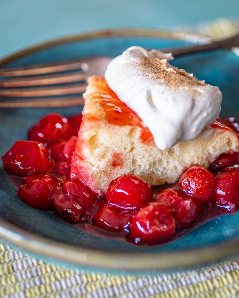 A slice of cherry upside down cake with whipped cream.
