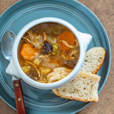Cock-a-leekie soup in a lion's head bowl with slices of bread, on a blue plate.
