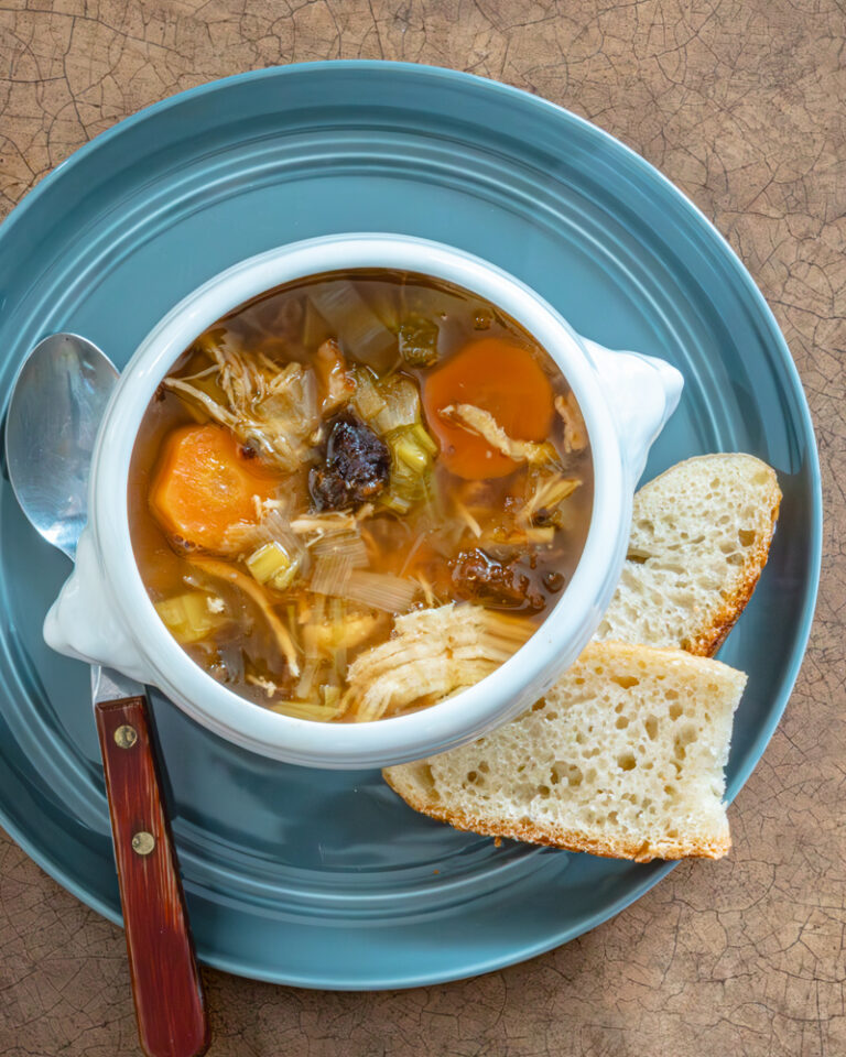 Cock-a-leekie soup in a lion's head bowl with slices of bread, on a blue plate.