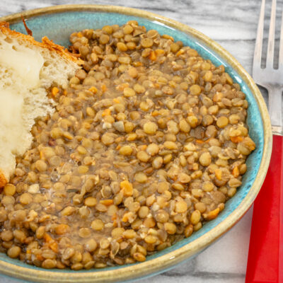 Bowl of cooked lentils with carrots and broth, with a piece of bread on the side.