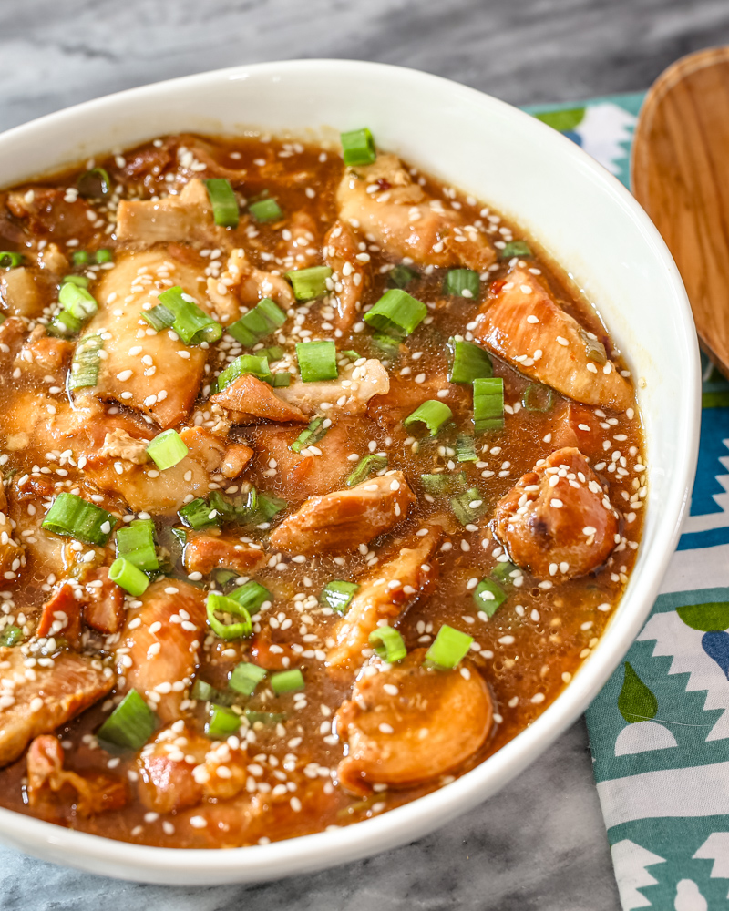 A serving bowl of honey sesame chicken thighs with a garnish of green onions and sesame seeds.