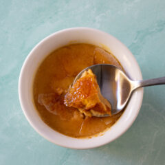 Pumpkin creme brulee in a ramekin with a spoon showing the cracked sugar top.