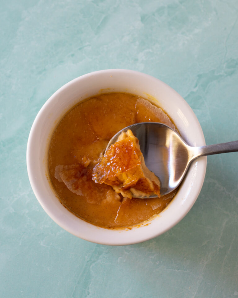 Pumpkin creme brulee in a ramekin with a spoon showing the cracked sugar top.