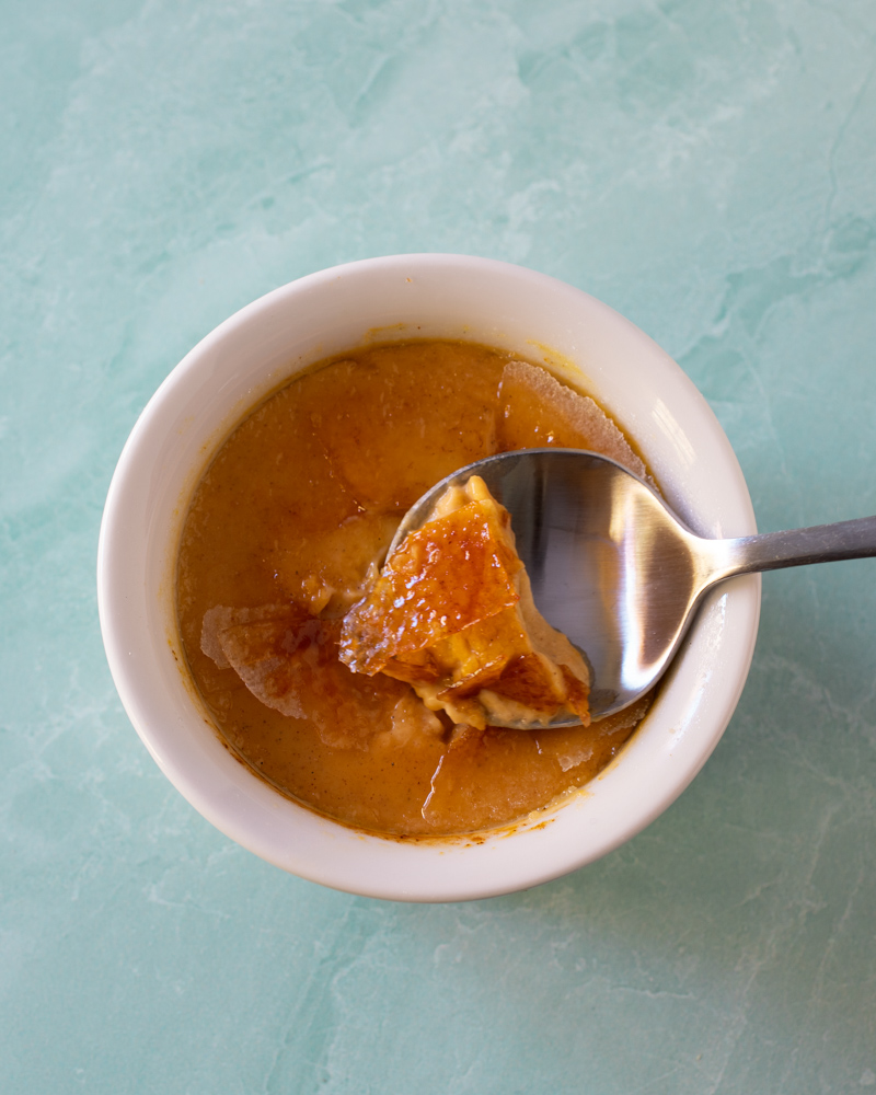 Pumpkin creme brulee in a ramekin with a spoon showing the cracked sugar top.