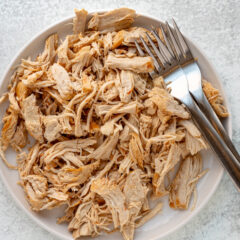 Shredded cooked chicken on a white plate with 2 forks.