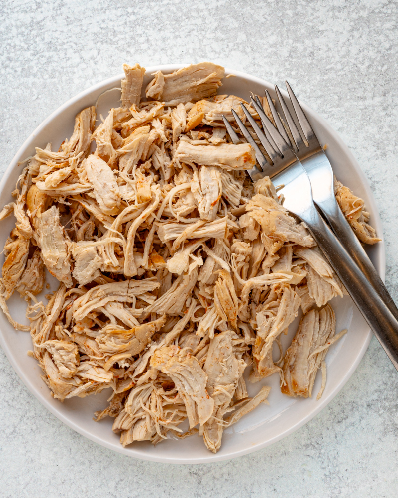 Shredded cooked chicken on a white plate with 2 forks.