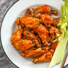 Spicy wings on a large enamel plate with celery sticks on the side.