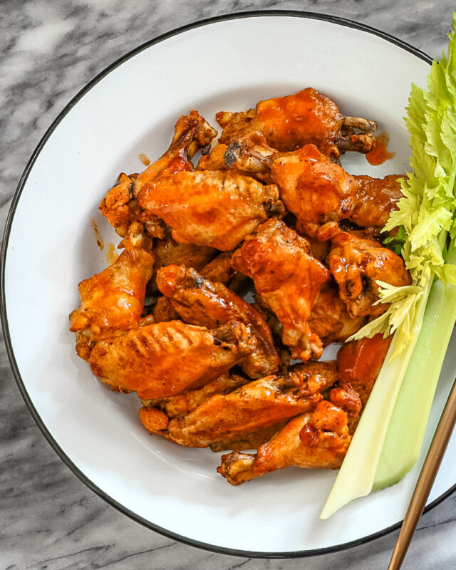 Spicy wings on a large enamel plate with celery sticks on the side.