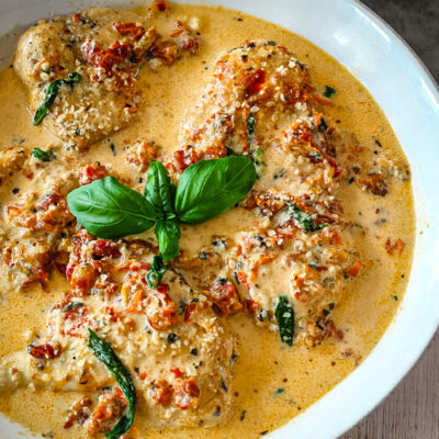 Creamy Tuscan chicken in a flavorful sauce with basil garnish on a white dish.