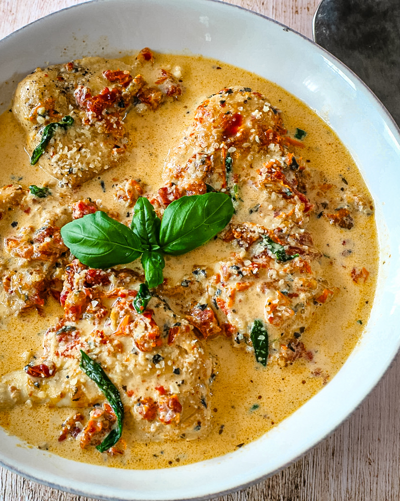 Creamy Tuscan chicken in a flavorful sauce with basil garnish on a white dish.