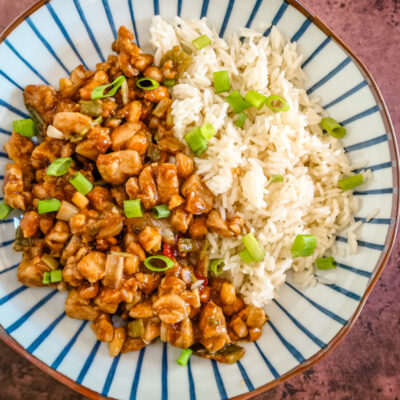A serving of kung pao chicken with rice and green onion garnish.