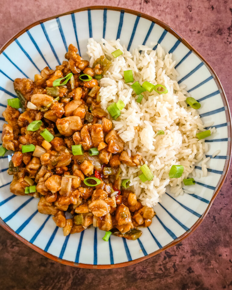 A serving of kung pao chicken with rice and green onion garnish.