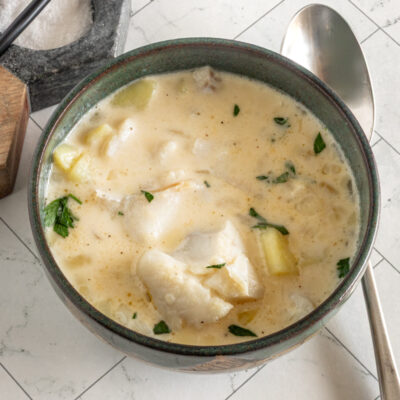 Creamy haddock chowder with herbs in a dark green bowl.