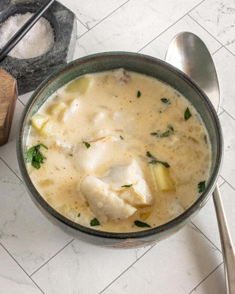 Creamy haddock chowder with herbs in a dark green bowl.