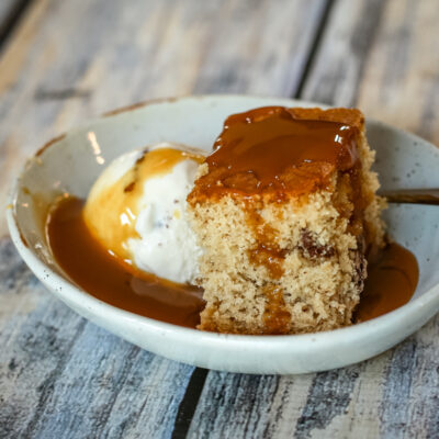 A slice of maple walnut snack cake with ice cream and caramel sauce.