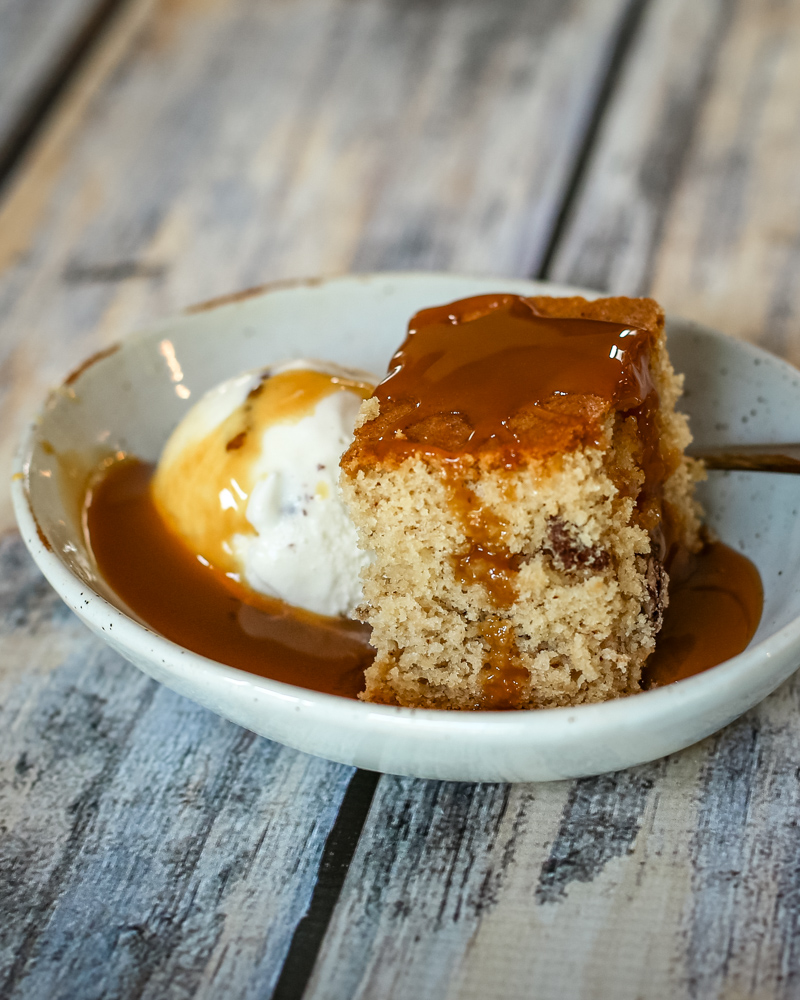 A slice of maple walnut snack cake with ice cream and caramel sauce.