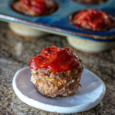 A meatloaf muffin with sauce on top, shown with more meatloaf muffins in the background.