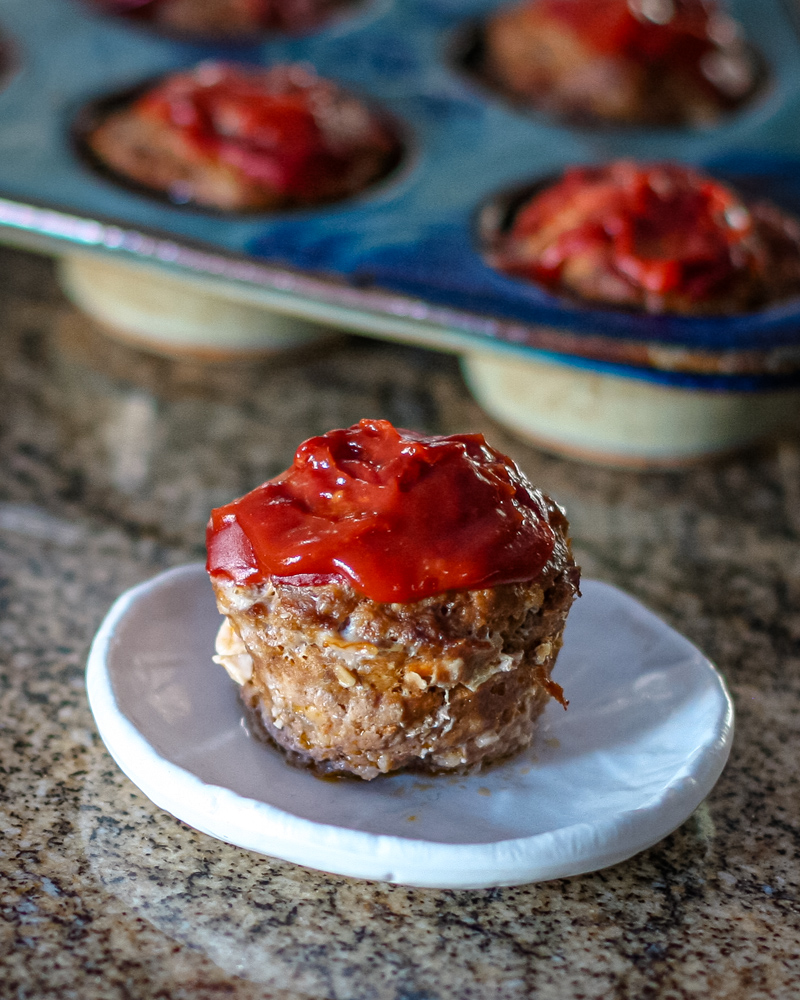 A meatloaf muffin with sauce on top, shown with more meatloaf muffins in the background.