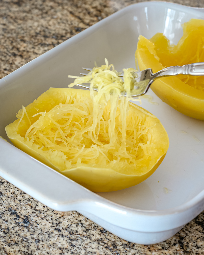 Spaghetti squash in a baking dish cooked in the microwave—strands lifted with a fork.