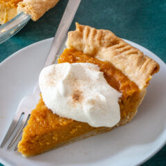 A slice of sweet potato pie on a plate with a dollop of whipped cream and cinnamon sugar.