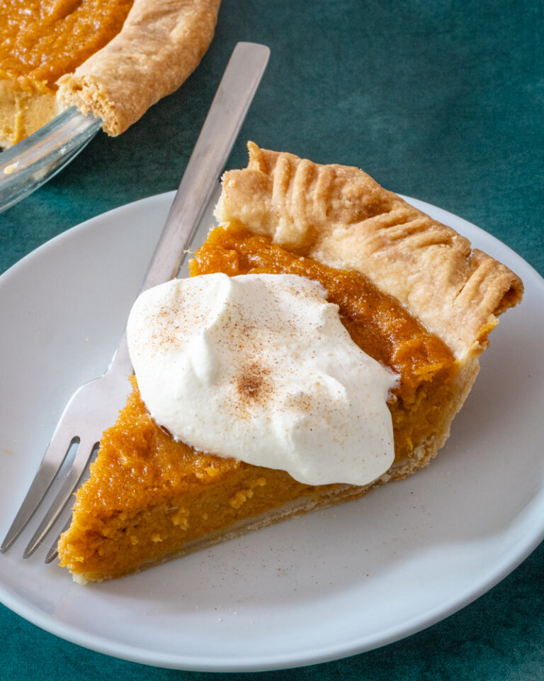 A slice of sweet potato pie on a plate with a dollop of whipped cream and cinnamon sugar.