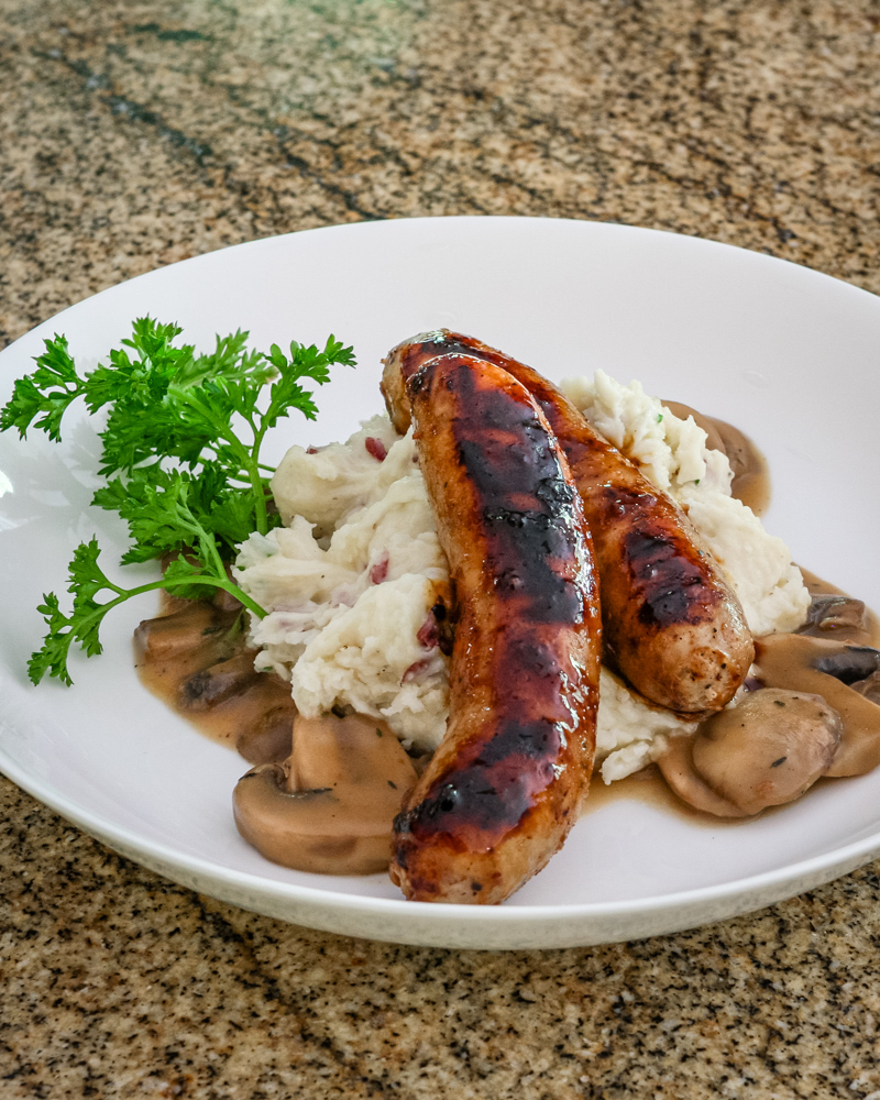 Mushroom sauce with beef stock, garlic, and a splash of beer shown with mashed potatoes and grilled sausages.