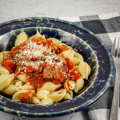 A wide bowl with Neapolitan sauce with sausage and tomatoes over pasta shells.