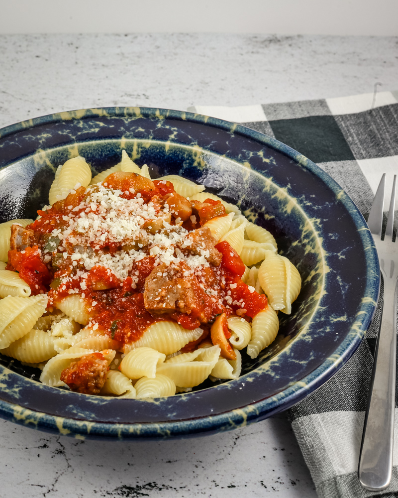 A wide bowl with Neapolitan sauce with sausage and tomatoes over pasta shells.