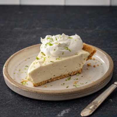 A slice of no-bake key lime cheesecake with whipped cream and lime zest.