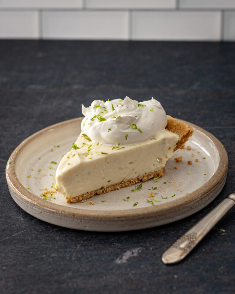 A slice of no-bake key lime cheesecake with whipped cream and lime zest.