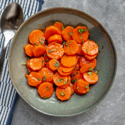 Sweet glazed carrots garnished with chopped herbs in a rustic bowl.