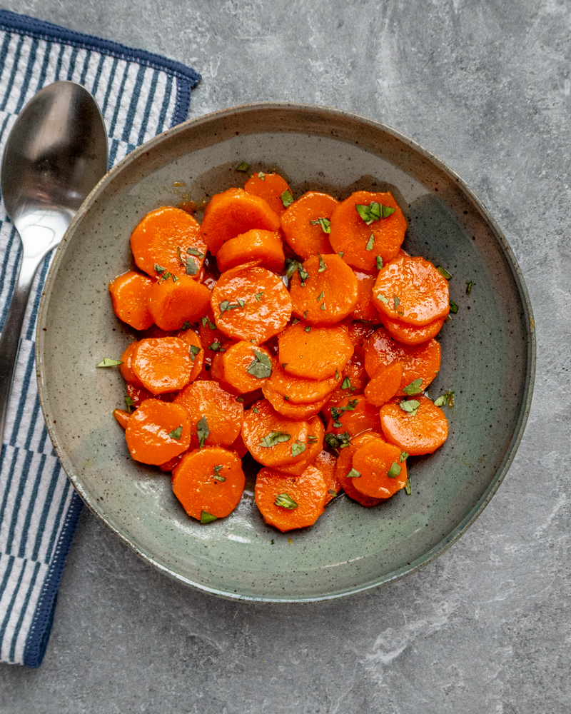 Sweet glazed carrots garnished with chopped herbs in a rustic bowl.