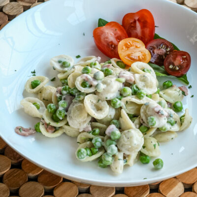 A pasta bowl with a dish of orecchiette with ham, peas, and Parmesan cheese.
