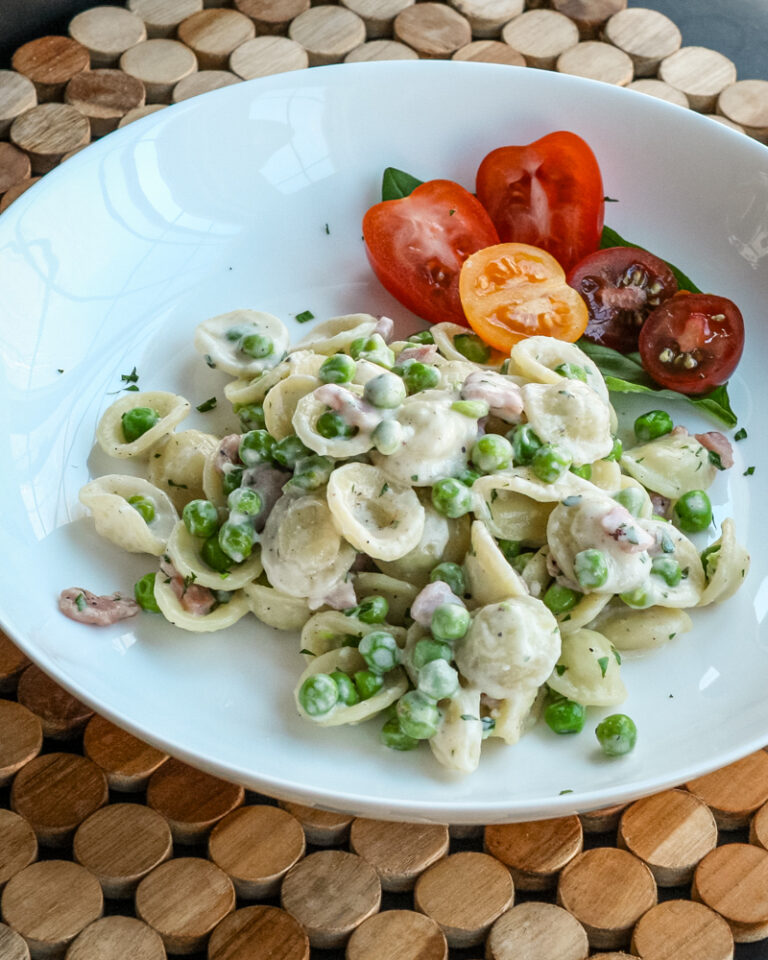 A pasta bowl with a dish of orecchiette with ham, peas, and Parmesan cheese.